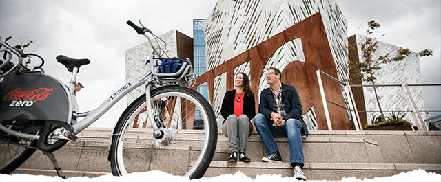 A couple sitting on zteps with a bike in the foreground. 